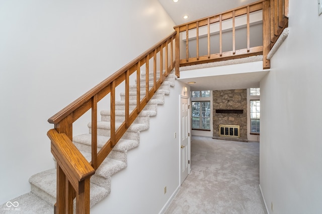 stairway featuring a stone fireplace, carpet floors, and a high ceiling