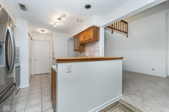 kitchen featuring tasteful backsplash, stainless steel fridge with ice dispenser, light carpet, sink, and kitchen peninsula