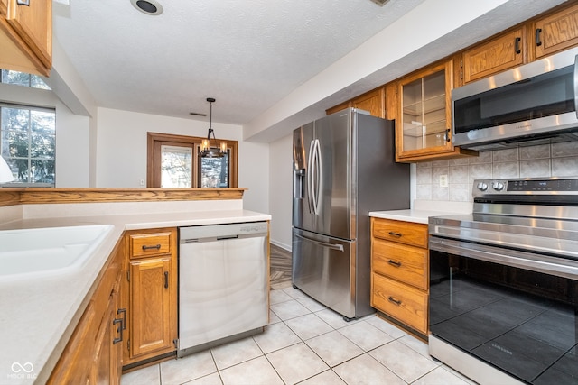 kitchen featuring appliances with stainless steel finishes, decorative light fixtures, light tile patterned floors, a textured ceiling, and decorative backsplash