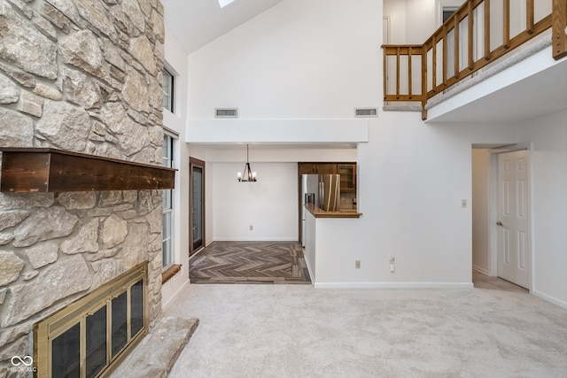 unfurnished living room with high vaulted ceiling, an inviting chandelier, light colored carpet, and a fireplace