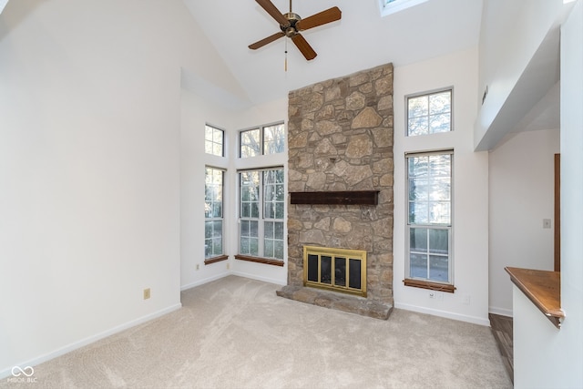 unfurnished living room featuring a fireplace, a high ceiling, a skylight, light colored carpet, and ceiling fan