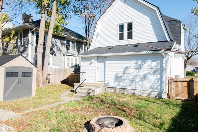 rear view of property featuring a yard, a storage unit, and an outdoor fire pit