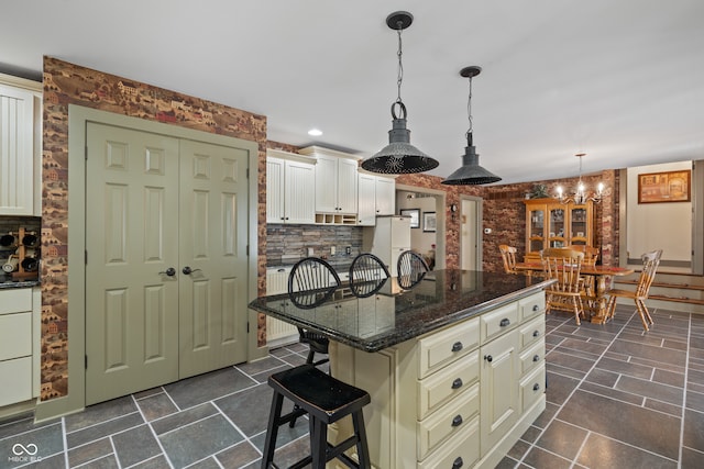 kitchen with dark stone counters, an inviting chandelier, a center island, hanging light fixtures, and a breakfast bar area