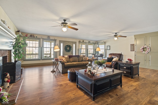 living room with a fireplace, a textured ceiling, ceiling fan, and dark wood-type flooring