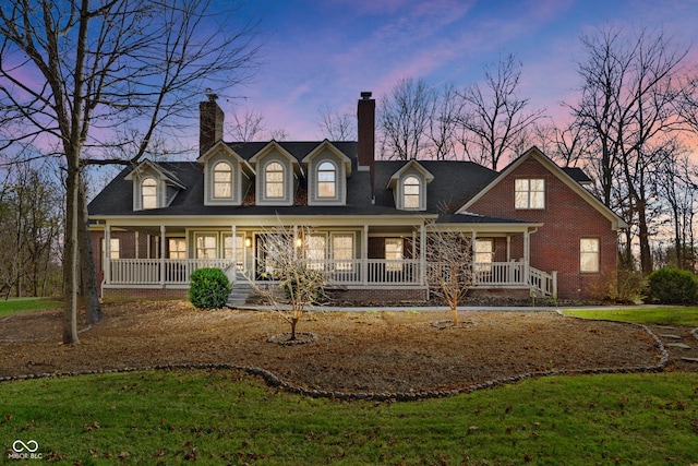 cape cod-style house with a lawn and covered porch