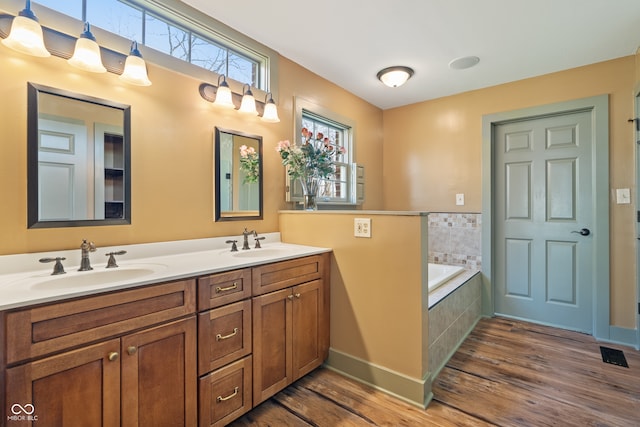 bathroom featuring wood-type flooring, vanity, and tiled tub