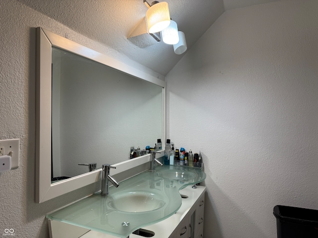 bathroom with a textured ceiling, vanity, and lofted ceiling