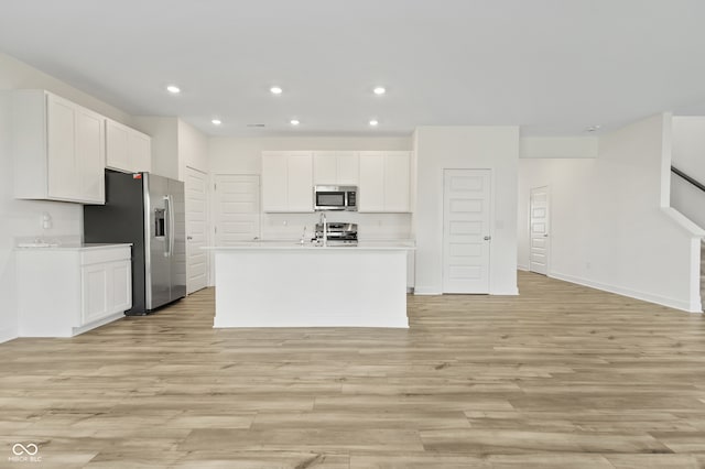 kitchen with appliances with stainless steel finishes, light wood-type flooring, a center island with sink, and white cabinetry