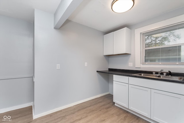 kitchen with white cabinetry, sink, beam ceiling, and light wood-type flooring