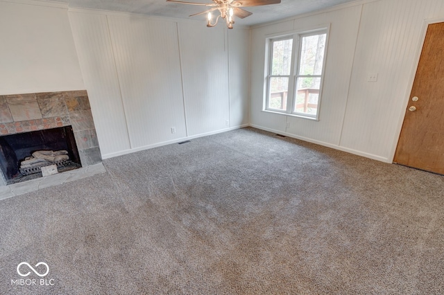 unfurnished living room with a tiled fireplace, ceiling fan, and carpet floors