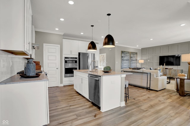 kitchen with stainless steel appliances, crown molding, pendant lighting, white cabinetry, and an island with sink