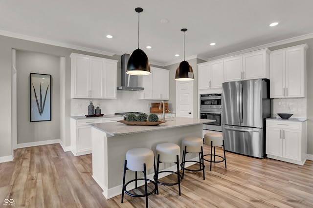 kitchen featuring appliances with stainless steel finishes, backsplash, wall chimney exhaust hood, white cabinetry, and an island with sink