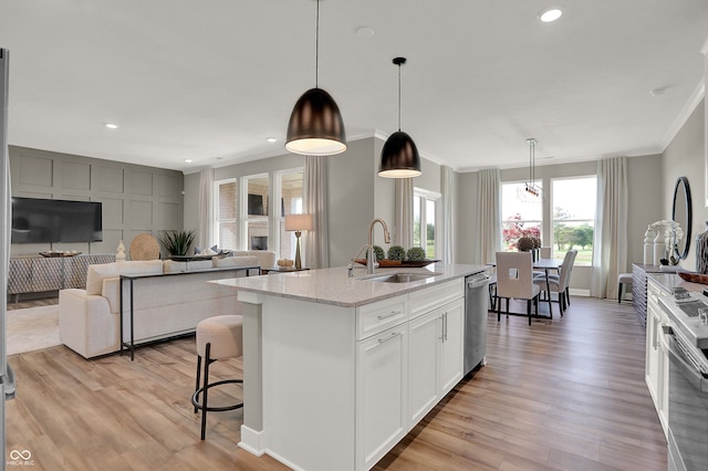 kitchen with sink, hanging light fixtures, an island with sink, light stone counters, and white cabinetry