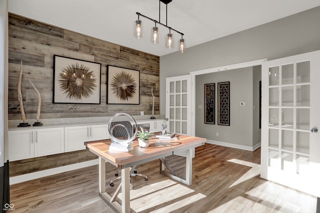 office space featuring french doors, light wood-type flooring, and wood walls