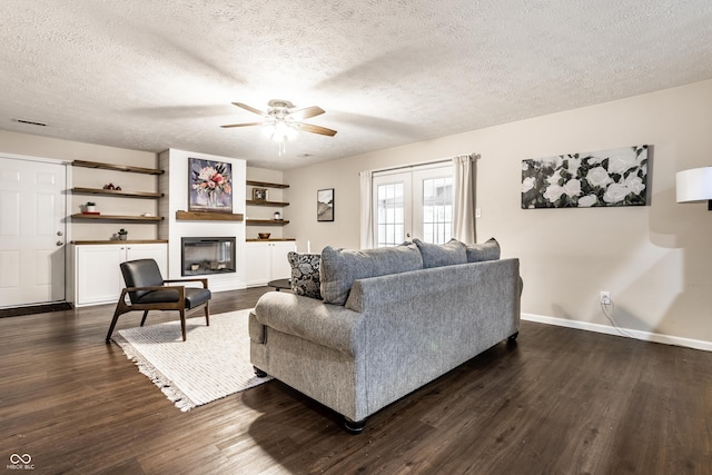 living area featuring a ceiling fan, baseboards, dark wood-type flooring, a textured ceiling, and a glass covered fireplace