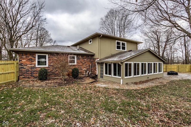 rear view of property with brick siding, fence, roof with shingles, a lawn, and a sunroom