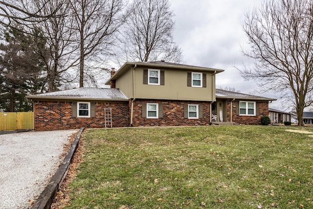 split level home with a front yard, fence, brick siding, and a chimney