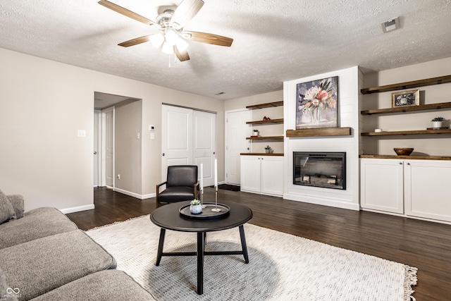 living area with a fireplace, a textured ceiling, dark wood-type flooring, and baseboards