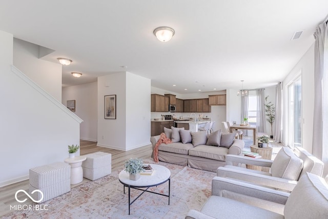 living room with an inviting chandelier, sink, and light hardwood / wood-style flooring