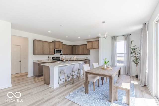 kitchen featuring a center island with sink, appliances with stainless steel finishes, hanging light fixtures, an inviting chandelier, and light hardwood / wood-style flooring