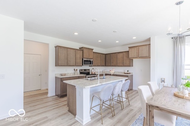 kitchen featuring an island with sink, sink, light hardwood / wood-style flooring, and appliances with stainless steel finishes