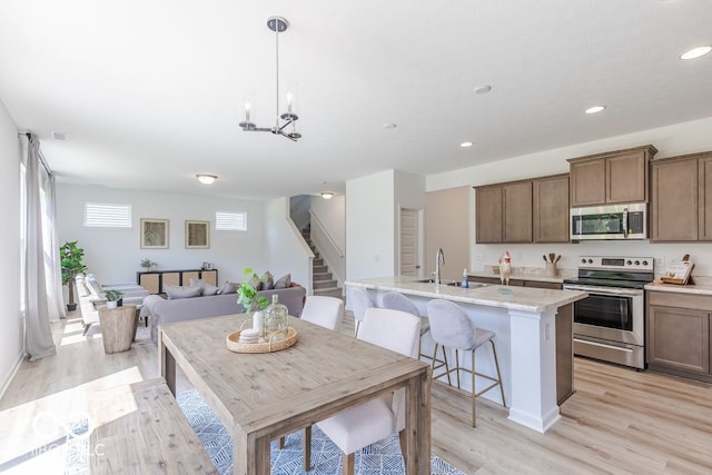 kitchen featuring stainless steel appliances, a center island with sink, sink, a breakfast bar, and light wood-type flooring