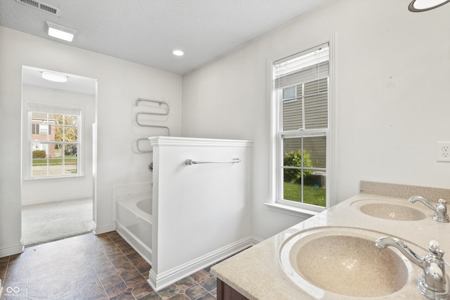 bathroom with a tub, a wealth of natural light, vanity, and a textured ceiling