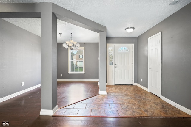 foyer entrance with a textured ceiling, dark hardwood / wood-style floors, and an inviting chandelier