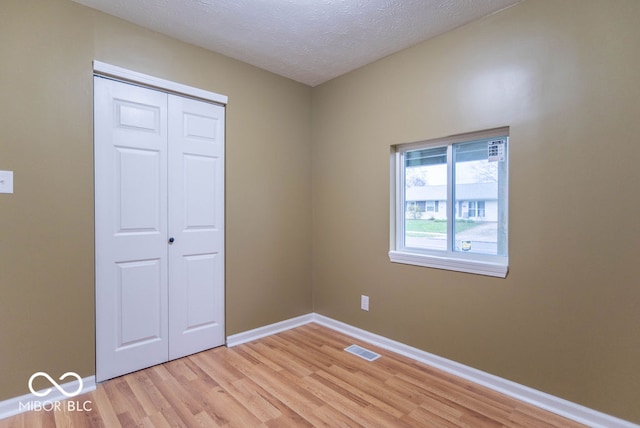 unfurnished bedroom with light wood-type flooring, a textured ceiling, and a closet