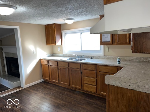 kitchen with a tiled fireplace, dark hardwood / wood-style flooring, a textured ceiling, sink, and range hood