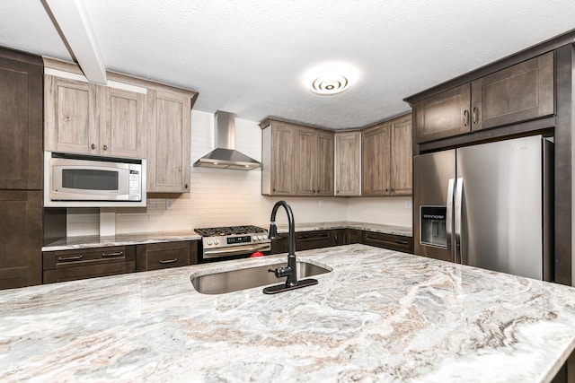 kitchen with appliances with stainless steel finishes, backsplash, light stone counters, wall chimney exhaust hood, and sink