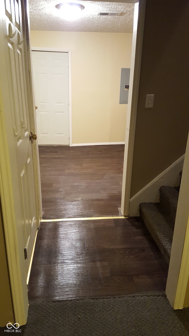 hall featuring a textured ceiling, electric panel, and dark wood-type flooring