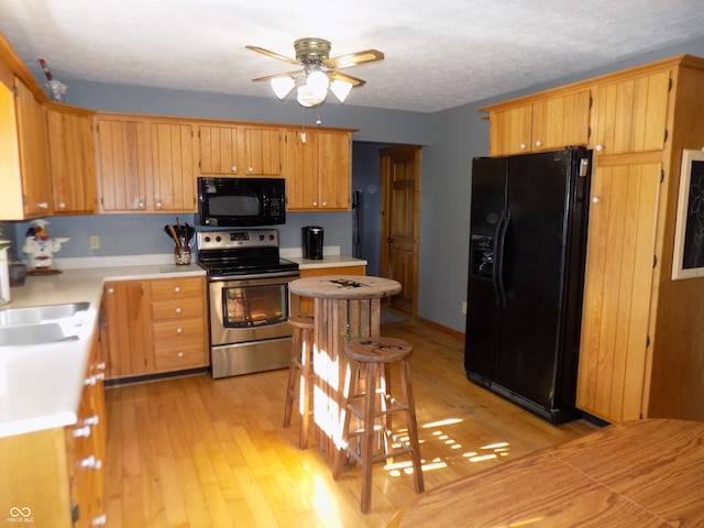 kitchen with sink, light hardwood / wood-style floors, ceiling fan, and black appliances