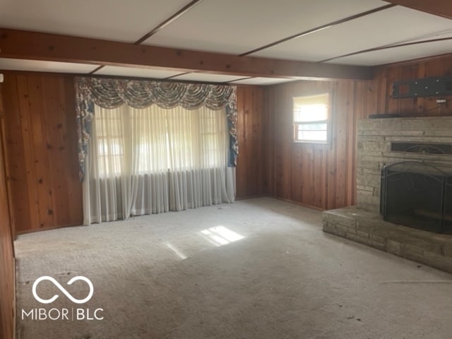 unfurnished living room with a stone fireplace, carpet flooring, wooden walls, and beam ceiling