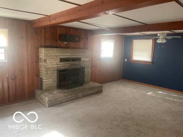 unfurnished living room featuring carpet, a fireplace, wooden walls, beamed ceiling, and ceiling fan