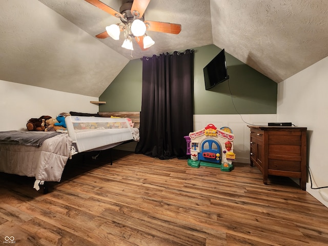 bedroom with hardwood / wood-style floors, lofted ceiling, a textured ceiling, and ceiling fan