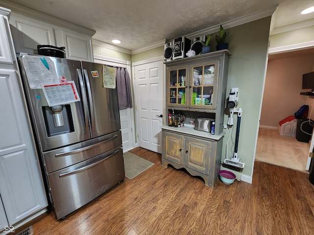 kitchen with wood-type flooring, a textured ceiling, crown molding, white cabinetry, and stainless steel fridge