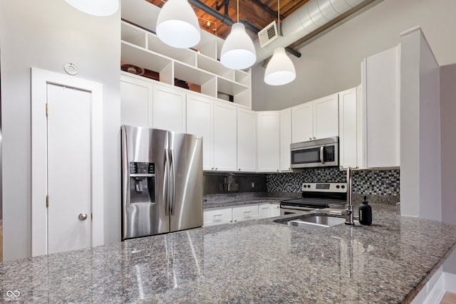 kitchen featuring appliances with stainless steel finishes, white cabinetry, hanging light fixtures, and dark stone counters