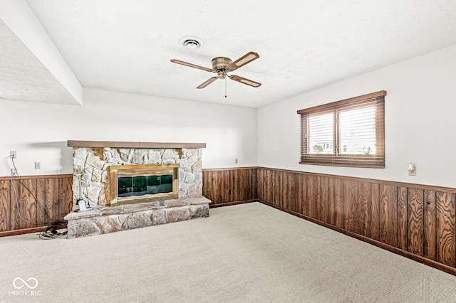 unfurnished living room with carpet flooring, wood walls, a fireplace, and a textured ceiling