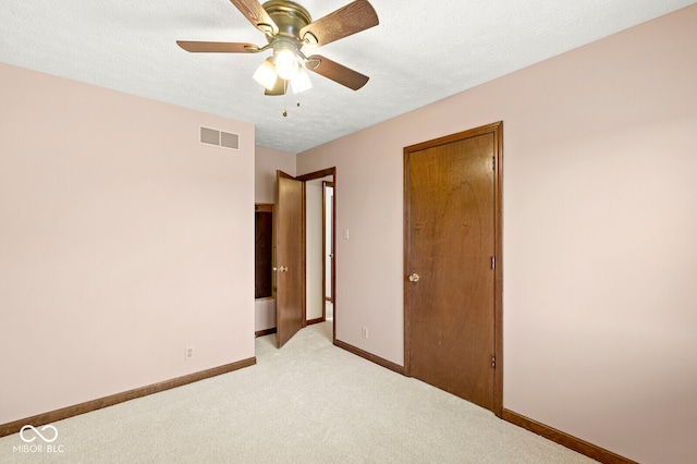 unfurnished bedroom featuring a textured ceiling, light colored carpet, and ceiling fan