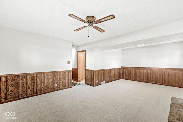 empty room featuring wooden walls, carpet floors, a textured ceiling, and ceiling fan