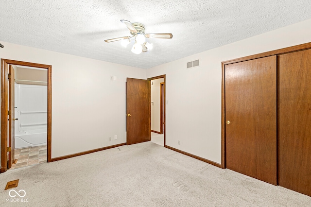 unfurnished bedroom featuring ensuite bath, a textured ceiling, light colored carpet, ceiling fan, and a closet