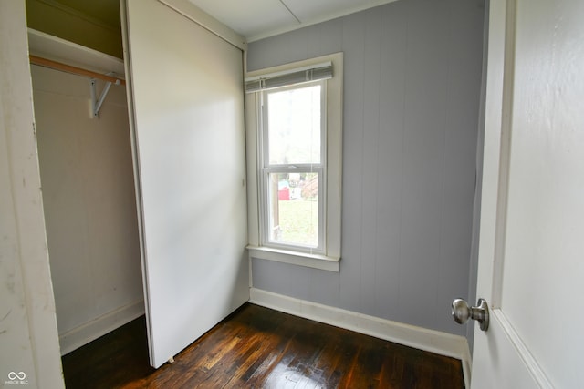 unfurnished bedroom featuring multiple windows, wood walls, a closet, and dark wood-type flooring