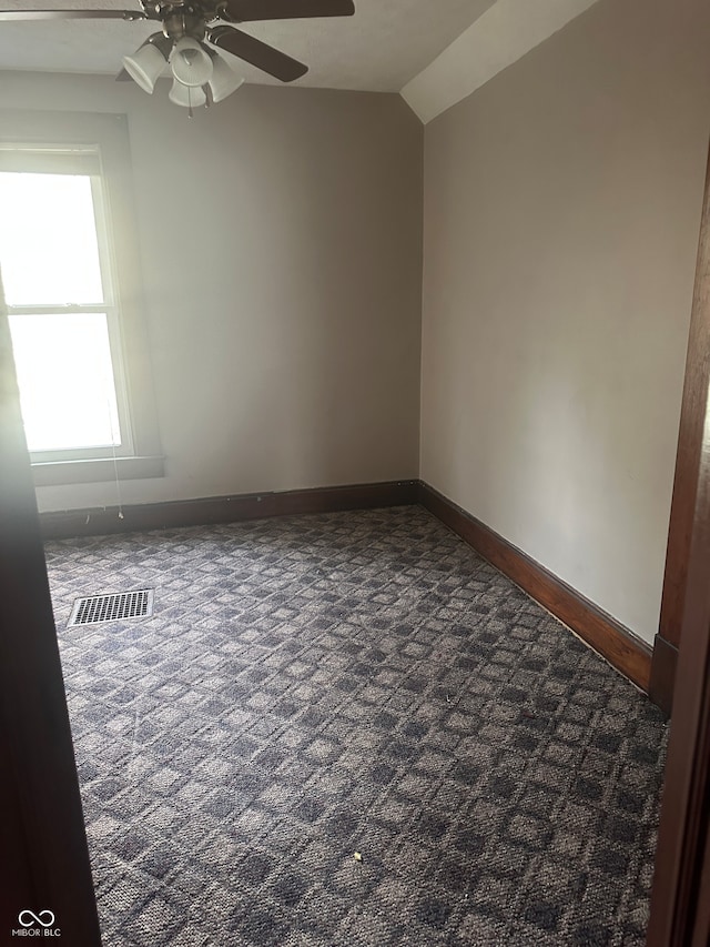 spare room with ceiling fan, dark carpet, and vaulted ceiling