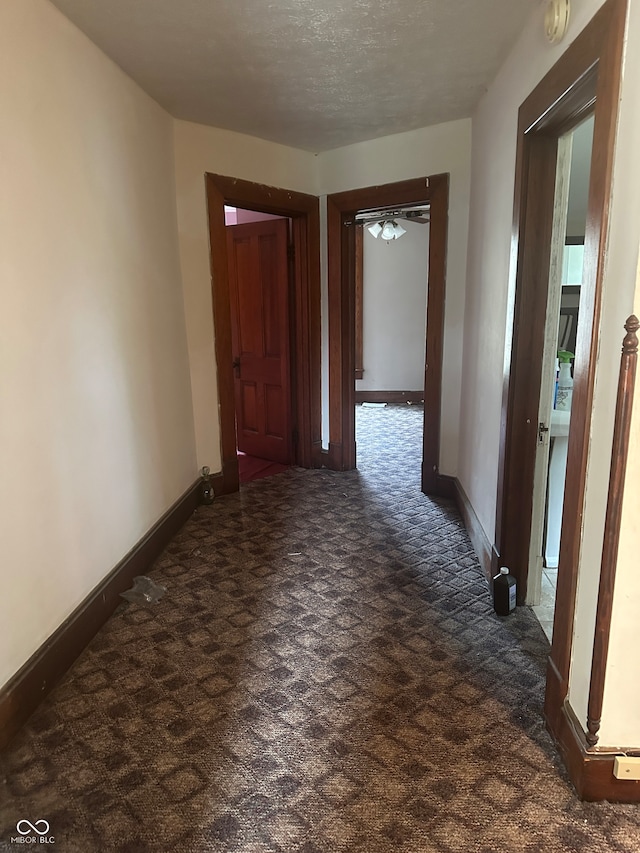 corridor featuring dark colored carpet and a textured ceiling