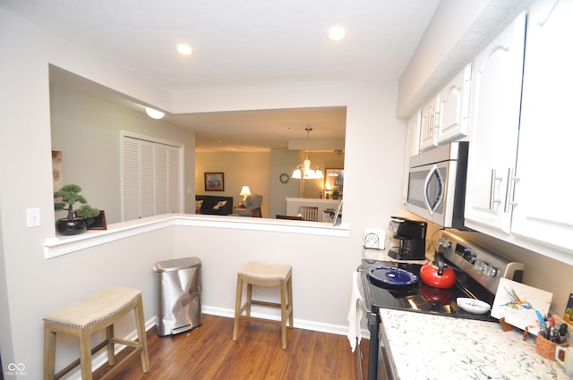 kitchen with appliances with stainless steel finishes, dark hardwood / wood-style flooring, a kitchen breakfast bar, an inviting chandelier, and white cabinets