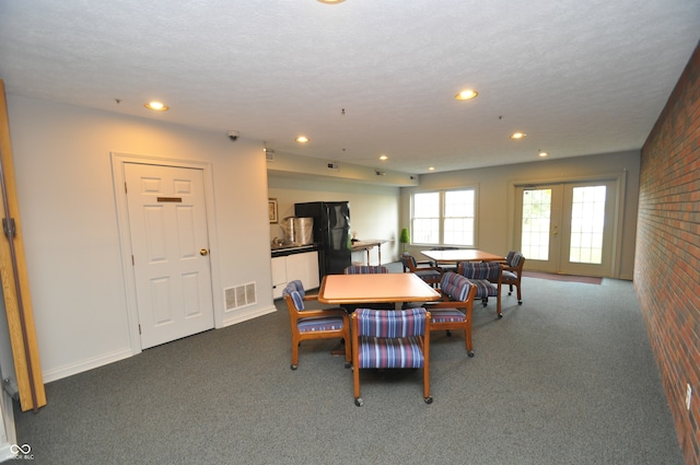 dining space featuring dark carpet, a textured ceiling, brick wall, and french doors