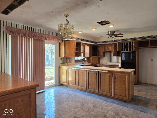 kitchen featuring kitchen peninsula, ceiling fan with notable chandelier, black microwave, and hanging light fixtures