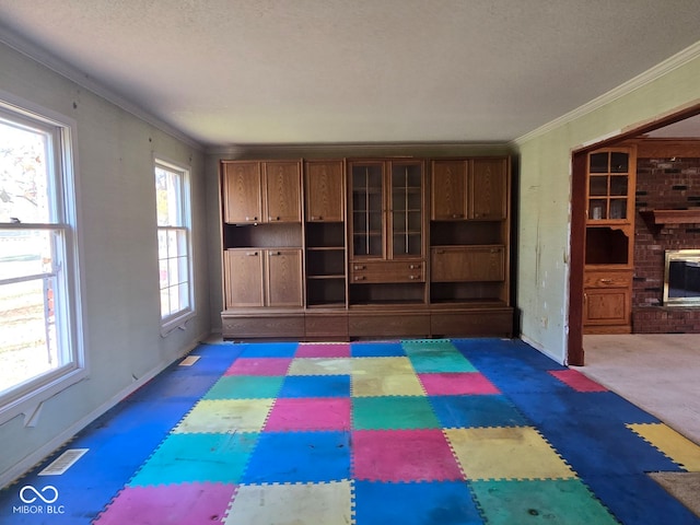 unfurnished living room with a brick fireplace, dark carpet, a textured ceiling, and ornamental molding