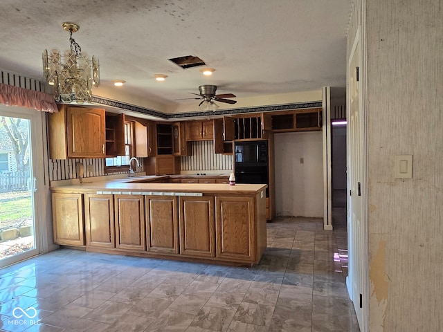 kitchen featuring black microwave, sink, kitchen peninsula, pendant lighting, and ceiling fan with notable chandelier